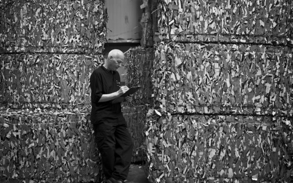 McLaren worker writing on clipboard in front of raw natural packaging materials in stacks