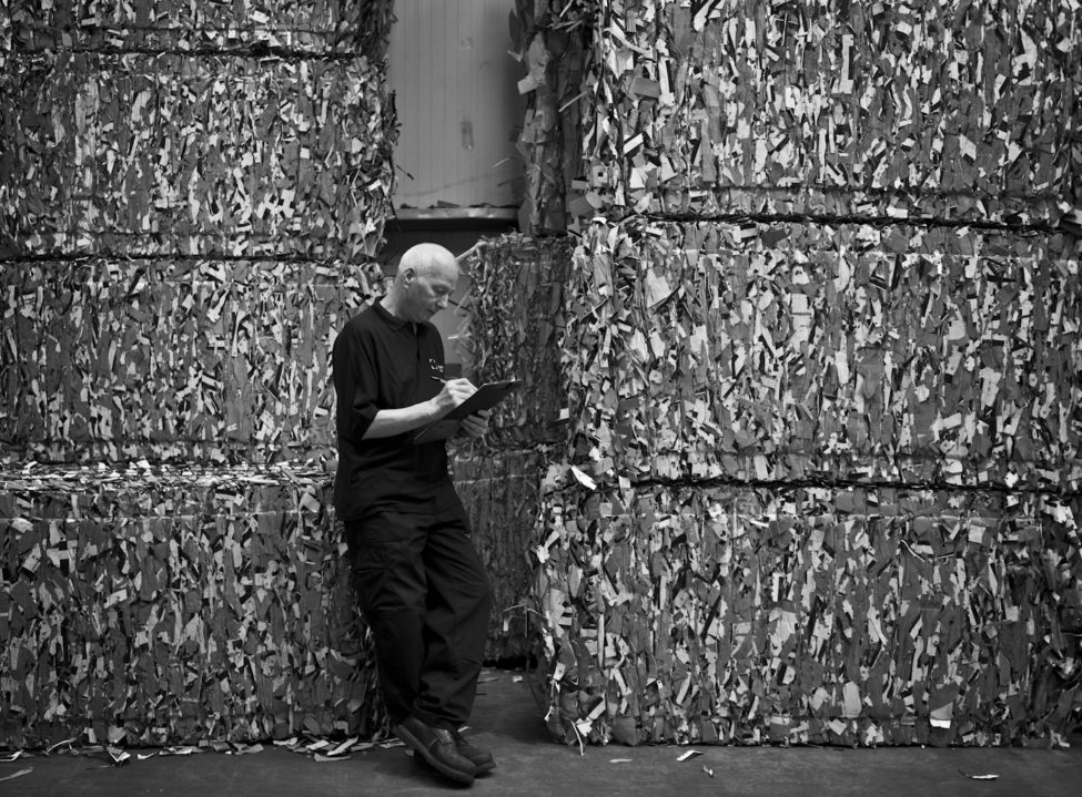 McLaren worker writing on clipboard in front of raw natural packaging materials in stacks